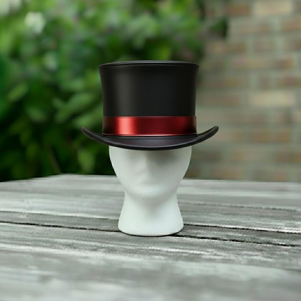 May include: A black top hat with a red band, displayed on a white mannequin head. The hat has a classic design with a slightly curved brim. The background features blurred green foliage and a brick wall.