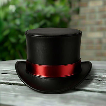 May include: A black top hat with a red band. The hat features a wide brim and a tall, cylindrical crown. The hat is made of a smooth material and rests on a wooden surface.
