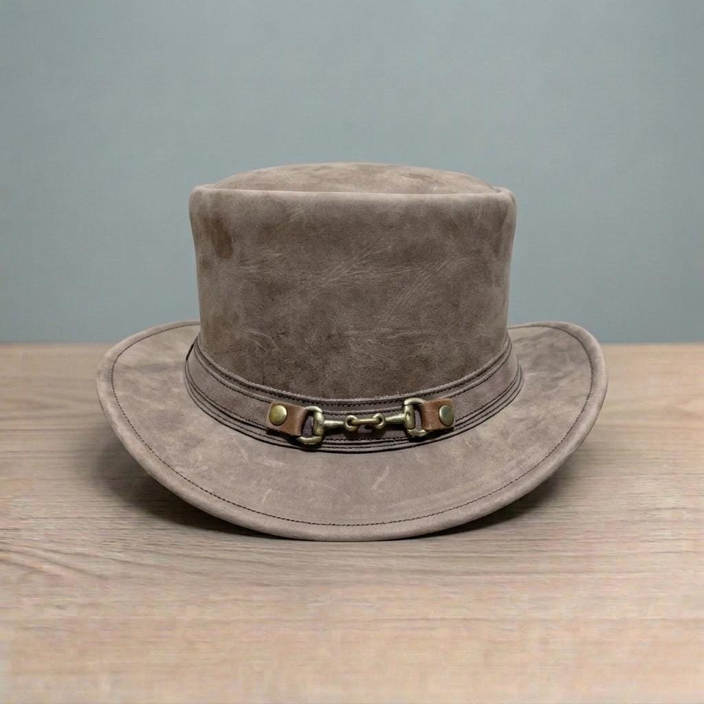 May include: A brown top hat with a wide brim. The hat has a leather band with a metal buckle detail. The hat is made of a soft, textured material and sits on a wooden surface.