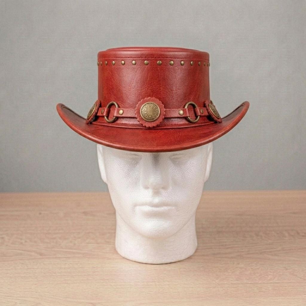 May include: A reddish-brown leather hat with a wide brim and a cylindrical crown. The hat features decorative brass-coloured studs around the crown and a band with circular accents and a central medallion. The hat is displayed on a white mannequin head.